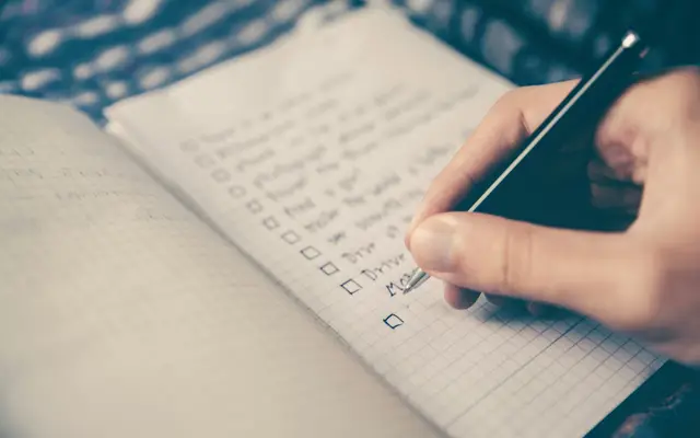 Pessoa anotando uma lista num caderno, como a lista para escolher o CRM da imobiliária