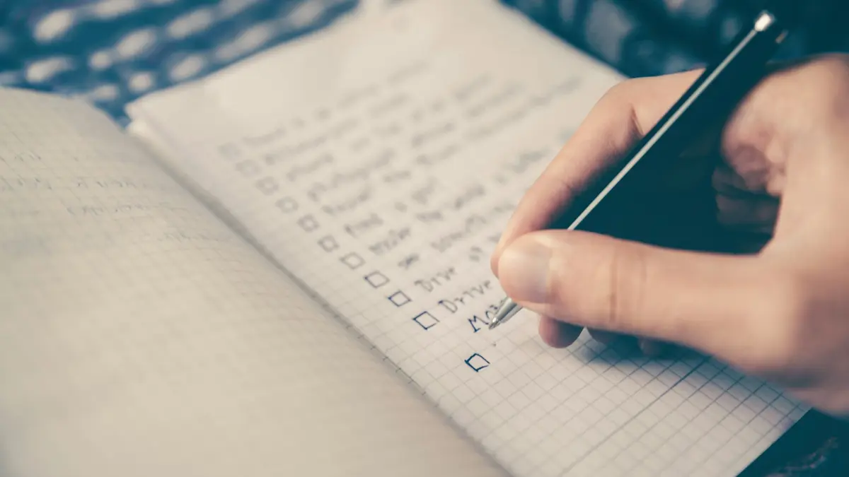 Pessoa anotando uma lista num caderno, como a lista para escolher o CRM da imobiliária