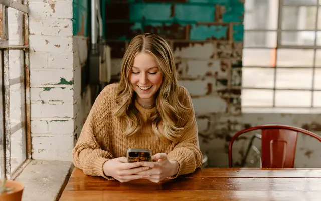 Mulher à mesa olhando o celular, conversando com um lead de imóvel no WhatsApp
