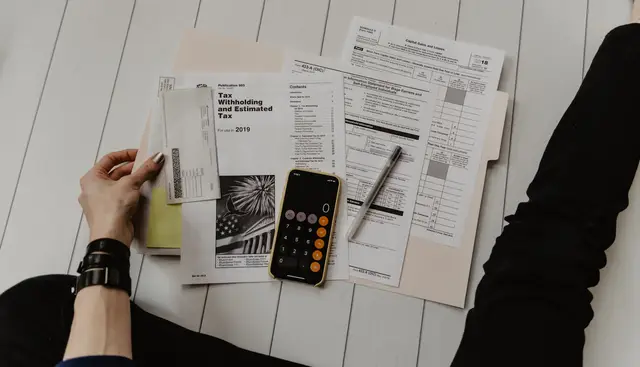 Pessoa segurando papel perto de caneta e calculadora, montando o DRE da imobiliária