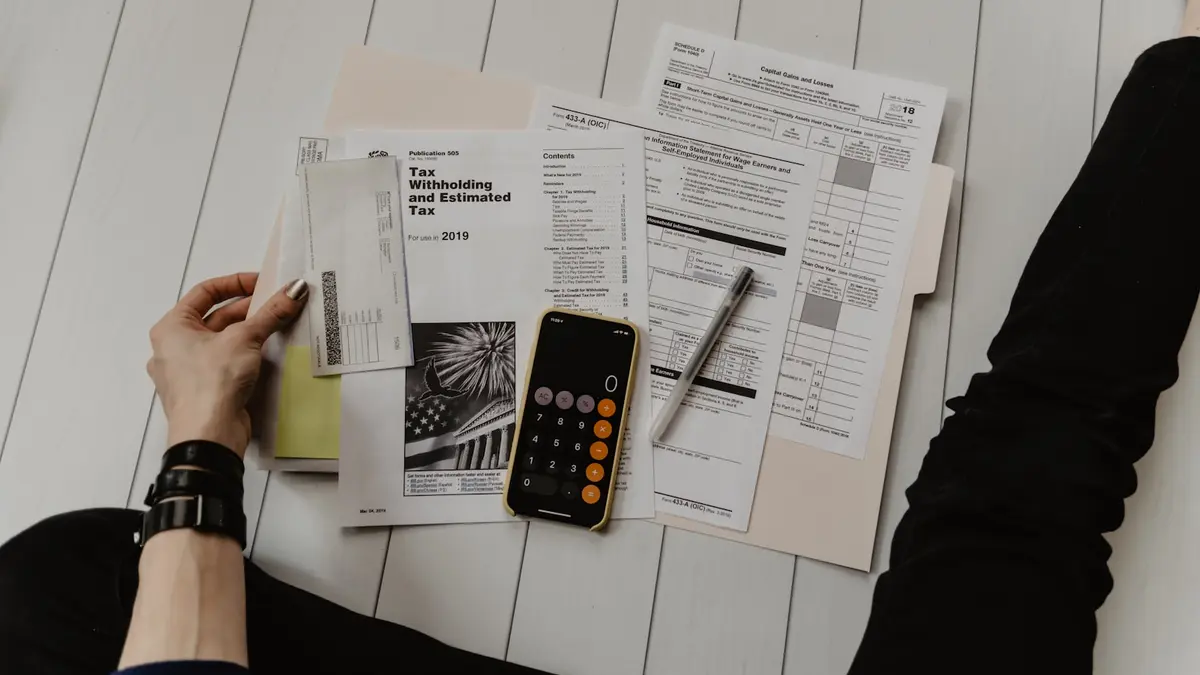 Pessoa segurando papel perto de caneta e calculadora, montando o DRE da imobiliária