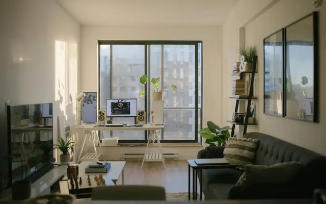 Sala de estar iluminada pelo sol, com escrivaninha, computador e sofá, bem fotografada