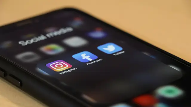 Celular sobre mesa de madeira, onde aparecem os anúncios do Meta Ads da imobiliária