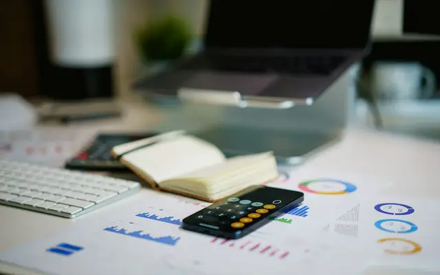 Escritório com celular e gráficos financeiros, calculando quanto custa um CRM imobiliário