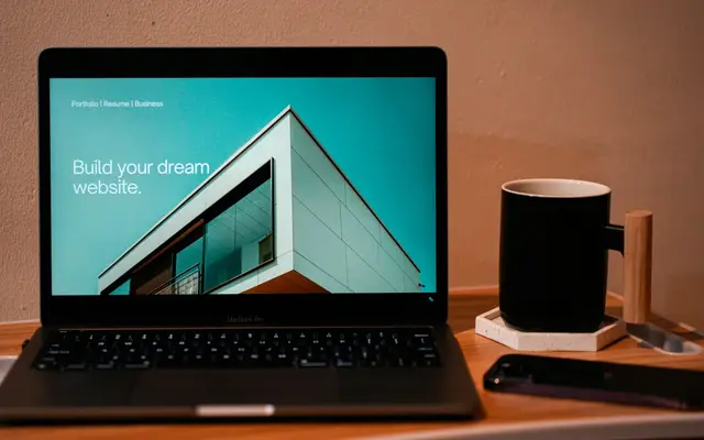 Notebook aberto sobre mesa de madeira, mostrando o site da imobiliária