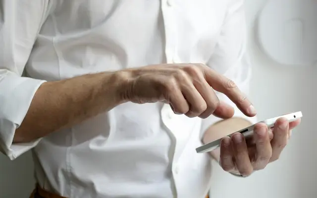 Pessoa segurando o celular, decidindo entre o WhatsApp oficial e o comum na imobiliária